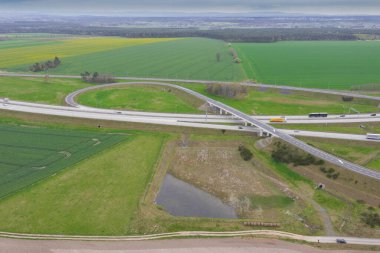 Uçsuz bucaksız, yeşil tarlalar ve çayırlar. Çerçevenin ortasında büyük bir iletişim kavşağı ve otobanda bir çatal var. Yüksek bir yerden bak. İHA 'dan fotoğraf..