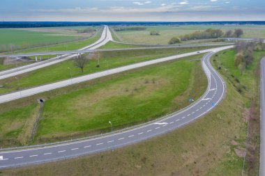 Uçsuz bucaksız, yeşil tarlalar ve çayırlar. Çerçevenin ortasında büyük bir iletişim kavşağı ve otobanda bir çatal var. Yüksek bir yerden bak. İHA 'dan fotoğraf..