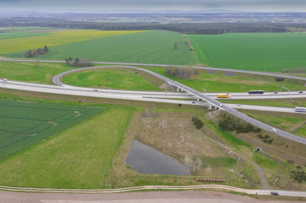 Uçsuz bucaksız, yeşil tarlalar ve çayırlar. Çerçevenin ortasında büyük bir iletişim kavşağı ve otobanda bir çatal var. Yüksek bir yerden bak. İHA 'dan fotoğraf..