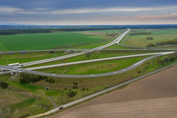 Uçsuz bucaksız, yeşil tarlalar ve çayırlar. Çerçevenin ortasında büyük bir iletişim kavşağı ve otobanda bir çatal var. Yüksek bir yerden bak. İHA 'dan fotoğraf..