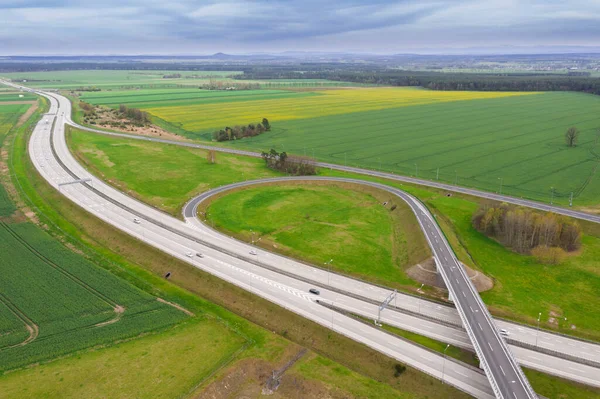 Uçsuz bucaksız, yeşil tarlalar ve çayırlar. Çerçevenin ortasında büyük bir iletişim kavşağı ve otobanda bir çatal var. Yüksek bir yerden bak. İHA 'dan fotoğraf..