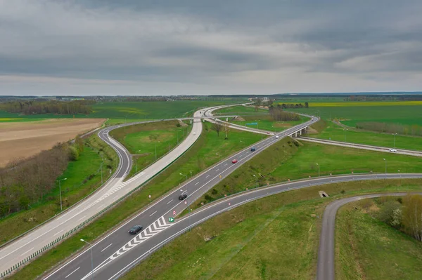 Uçsuz bucaksız, yeşil tarlalar ve çayırlar. Çerçevenin ortasında büyük bir iletişim kavşağı ve otobanda bir çatal var. Yüksek bir yerden bak. İHA 'dan fotoğraf..