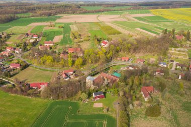 Yukarıdan görülen tarlalar ve çayırlar boyunca uzanan toprak bir yol. İHA 'dan bir fotoğraf. Uzaktan yakındaki bir köyün binalarını görebilirsin..
