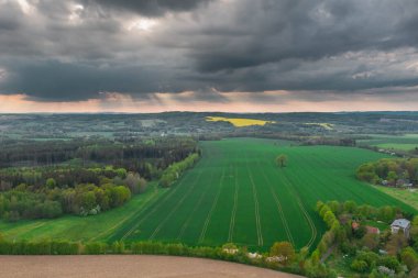 Sudeten Upland 'da. Tarıma elverişli tarlalar, çayırlar ve ormanlarla kaplı dalgalı bir arazi. Uzaktan tepeleri görebilirsin. Gökyüzü kısmen kara ve yağmurlu bulutlarla kaplı. İHA 'dan fotoğraf..