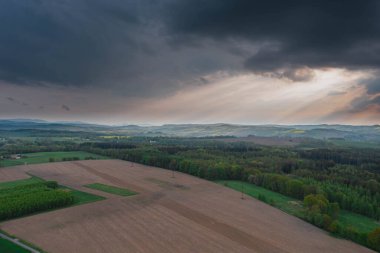 Sudeten Upland 'da. Tarıma elverişli tarlalar, çayırlar ve ormanlarla kaplı dalgalı bir arazi. Uzaktan tepeleri görebilirsin. Gökyüzü kısmen kara ve yağmurlu bulutlarla kaplı. İHA 'dan fotoğraf..