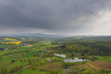 Sudeten Upland 'da. Tarıma elverişli tarlalar, çayırlar ve ormanlarla kaplı dalgalı bir arazi. Uzaktan tepeleri görebilirsin. Gökyüzü kısmen kara ve yağmurlu bulutlarla kaplı. İHA 'dan fotoğraf..