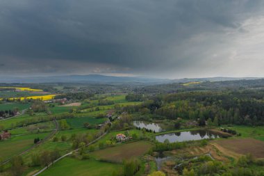 Sudeten Upland 'da. Tarıma elverişli tarlalar, çayırlar ve ormanlarla kaplı dalgalı bir arazi. Uzaktan tepeleri görebilirsin. Gökyüzü kısmen kara ve yağmurlu bulutlarla kaplı. İHA 'dan fotoğraf..