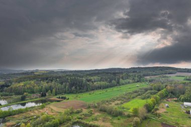 Sudeten Upland 'da. Tarıma elverişli tarlalar, çayırlar ve ormanlarla kaplı dalgalı bir arazi. Uzaktan tepeleri görebilirsin. Gökyüzü kısmen kara ve yağmurlu bulutlarla kaplı. İHA 'dan fotoğraf..