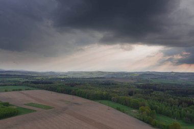 Sudeten Upland 'da. Tarıma elverişli tarlalar, çayırlar ve ormanlarla kaplı dalgalı bir arazi. Uzaktan tepeleri görebilirsin. Gökyüzü kısmen kara ve yağmurlu bulutlarla kaplı. İHA 'dan fotoğraf..