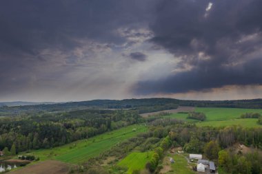 Sudeten Upland 'da. Tarıma elverişli tarlalar, çayırlar ve ormanlarla kaplı dalgalı bir arazi. Uzaktan tepeleri görebilirsin. Gökyüzü kısmen kara ve yağmurlu bulutlarla kaplı. İHA 'dan fotoğraf..