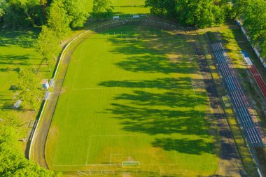 Bir taşra stadyumu. Merkezde çimlerle kaplı bir futbol sahası, koşu pisti ve taraftarlar için küçük bir stand var. İnsansız hava aracından görüntüle.