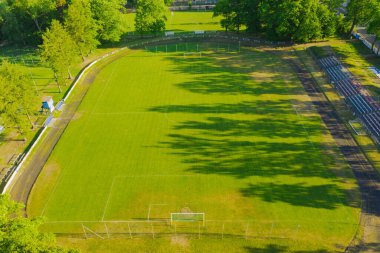 Bir taşra stadyumu. Merkezde çimlerle kaplı bir futbol sahası, koşu pisti ve taraftarlar için küçük bir stand var. İnsansız hava aracından görüntüle.