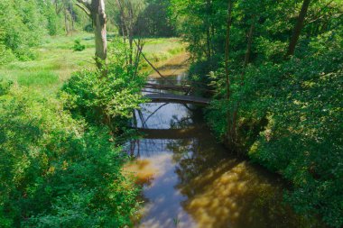 Lowland small river. It's a sunny day. The shores are covered with grass. There is a footbridge over the river. It's a sunny day. Photo from the drone.