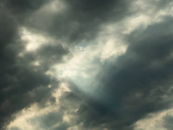 The sky is covered with gray clouds. Between the clouds there are gaps through which you can see the blue of the sky and streaks of light cut through.