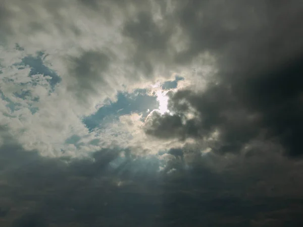 The sky is covered with gray clouds. Between the clouds there are gaps through which you can see the blue of the sky and streaks of light cut through.
