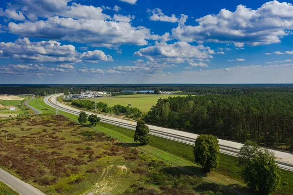 A vast plain covered with a green pine forest. Among the trees, you can see a two-lane concrete road. One of the road lanes is under construction. Photo from the drone.