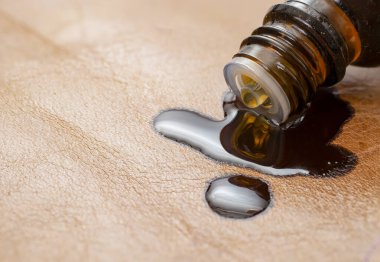 Esaslı bir yağ şişesi içeriğini kahverengi deri bir yüzeye döküyor. Deri mobilyalar makro konsepti mahvediyor.