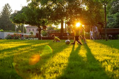 Odaklanamamak, bulanıklaşmak çocuklar, parkta güneş batarken çimenlerde futbol oynamak. Lens ve sarı ışık da mevcut. 