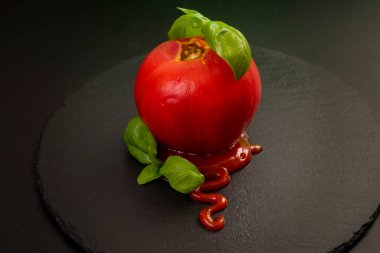 Ketçap ve fesleğen yapraklı soyulmuş domates, siyah bir taşın üzerine izole edilmiş.