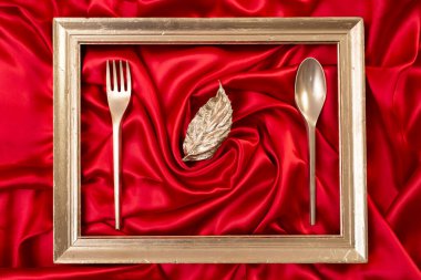 Altın çerçeve çatal bıçak takımı ve kırmızı saten arka planda kurumuş bir yaprak.