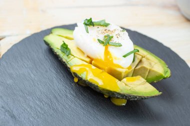 Avokadoda taze soğanlı haşlanmış yumurta, siyah taş levha, fayans arka plan, kenar görüş.