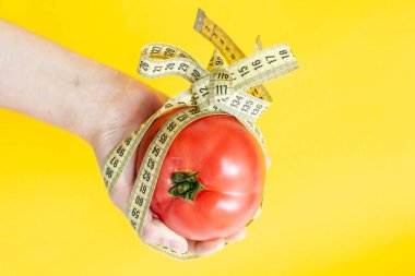 Bir kadının eli domates tutuyor, mezura yayıyla bağlanmış, sarı arka planda izole edilmiş.. 