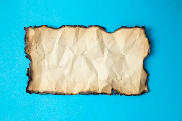 Vintage crumpled paper burned, close up isolated on blue background