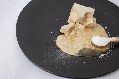Dissolving fresh yeast with sugar on a black plate. Close up side view