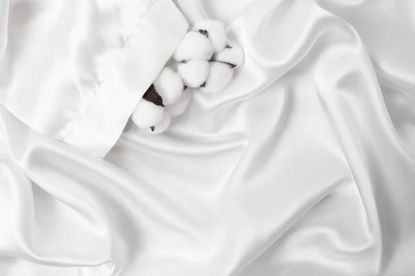 Cotton flowers in a white satin robe sleeve. Silky smooth product mockup for display. Flat lay close up