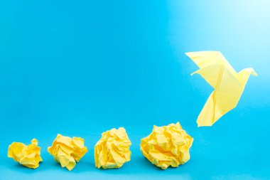 Sarı buruşmuş kağıt toplar ve mavi arkaplanda bir origami güvercini.