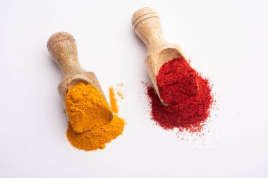 Tahta bir kepçenin içindeki zerdeçal ve kırmızı biber tozu ya da beyaz bir arka planda kaşık.
