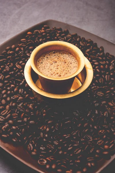 South Indian Filter coffee served in a traditional tumbler or cup over roasted raw beans