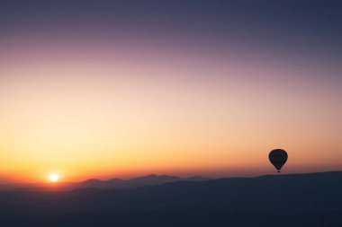 Sıcak hava balonlu manzara. Güneş doğarken gökyüzüne yükselen siyah siluet. Arka planda güzel yüksek dağ manzarası var.