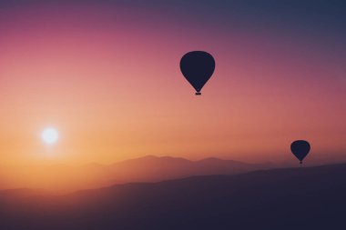 Sıcak hava balonlu manzara. Güneş doğarken gökyüzüne yükselen siyah siluet. Arka planda güzel yüksek dağ manzarası var.