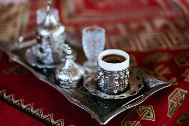 Geleneksel metal bardaklarda servis edilen Türk kahvesine yakın çekim ve bir restoranda gümüş tepside bir bardak su