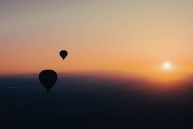 Sıcak hava balonlu manzara. Güneş doğarken gökyüzüne yükselen siyah siluet. Arka planda güzel yüksek dağ manzarası var.