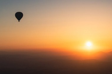 Sıcak hava balonlu manzara. Güneş doğarken gökyüzüne yükselen siyah siluet. Arka planda güzel yüksek dağ manzarası var.