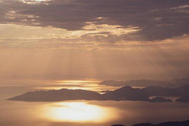 Türkiye 'de yaz mevsiminde Oludeniz Mavi Göl kıyısında gün batımında Akdeniz üzerinde yükselen yüksek dağların Babadag zirvesinden yükselen dikey hava manzarası