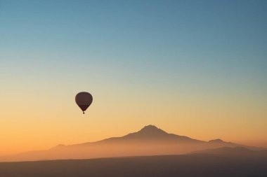 Güneşin doğuşuyla birlikte gökyüzüne yükselen sıcak hava balonu silüetiyle manzara. Arkaplanda erciyes dağının zirvesi sabah sisi ile kaplıydı.