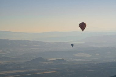 Güneşin doğuşuyla birlikte gökyüzüne yükselen uzak sıcak hava balonları ile yatay manzara. Sabah sisiyle kaplı güzel Kapadokya vadisi manzarası.