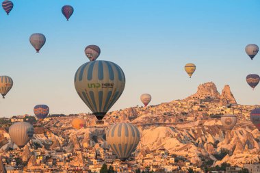 GOREME, TURKEY - 5 AĞUSTOS 2021: Kapadokya 'daki Goreme şehrinin üzerinde sabah ışığında Uchisar Kalesi' nin uzak arkaplanda uçuşan renkli sıcak hava balonları
