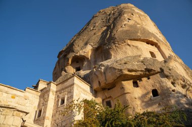 UCHISAR, TURKEY - 4 AĞUSTOS 2021: Uchisar Kalesi şatosundaki mağara evleri Kapadokyaca antik mimarisi ile günbatımında mavi gökyüzüne karşı
