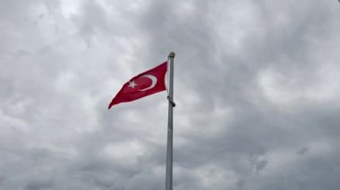 Türkiye 'nin ulusal bayrağına yakın çekim güçlü bir rüzgarla dalgalanırken, arka planda fırtına bulutlu gökyüzü