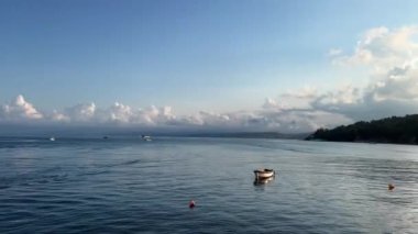 Sakin bir denizde, ufukta bulutlardan oluşan bir manzarayla kıyıya demir atmış yalnız ahşap bir kayık manzarası.
