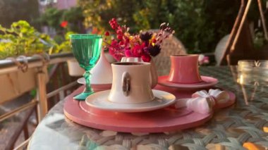 Geleneksel Türk kahve fincanlarının ön görüntüsü dışarıda su çiçekleri ve günbatımında cam masada romantik bir tatlı ile servis ediliyor.