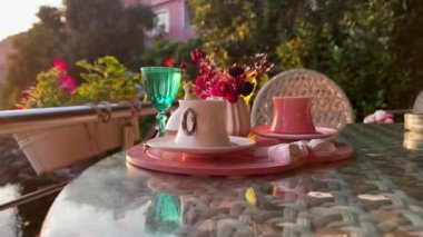 Geleneksel Türk kahve fincanlarının ön görüntüsü dışarıda su çiçekleri ve günbatımında cam masada romantik bir tatlı ile servis ediliyor.