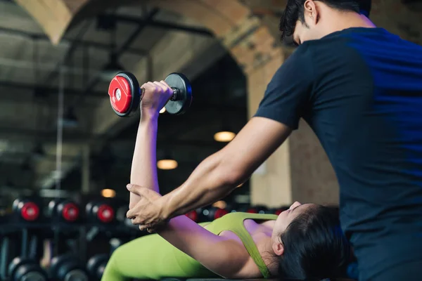 Selective focus, Personal trainer coach helping young female lifting bench press workout with dumbbell in fitness gym. Sport people exercise active in healthy lifestyle.