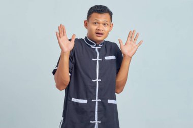 Gri arka planda karate giyen şaşırmış Asyalı genç adamın portresi.