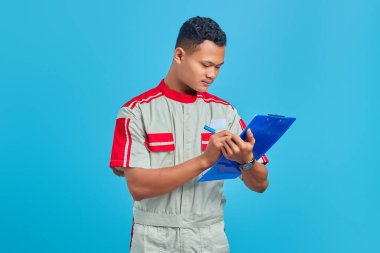 Tamirci üniforması giyen neşeli Asyalı yakışıklı adam. Not alıyor.