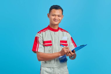 Tamirci üniforması giyen neşeli Asyalı yakışıklı adam. Not alıyor.